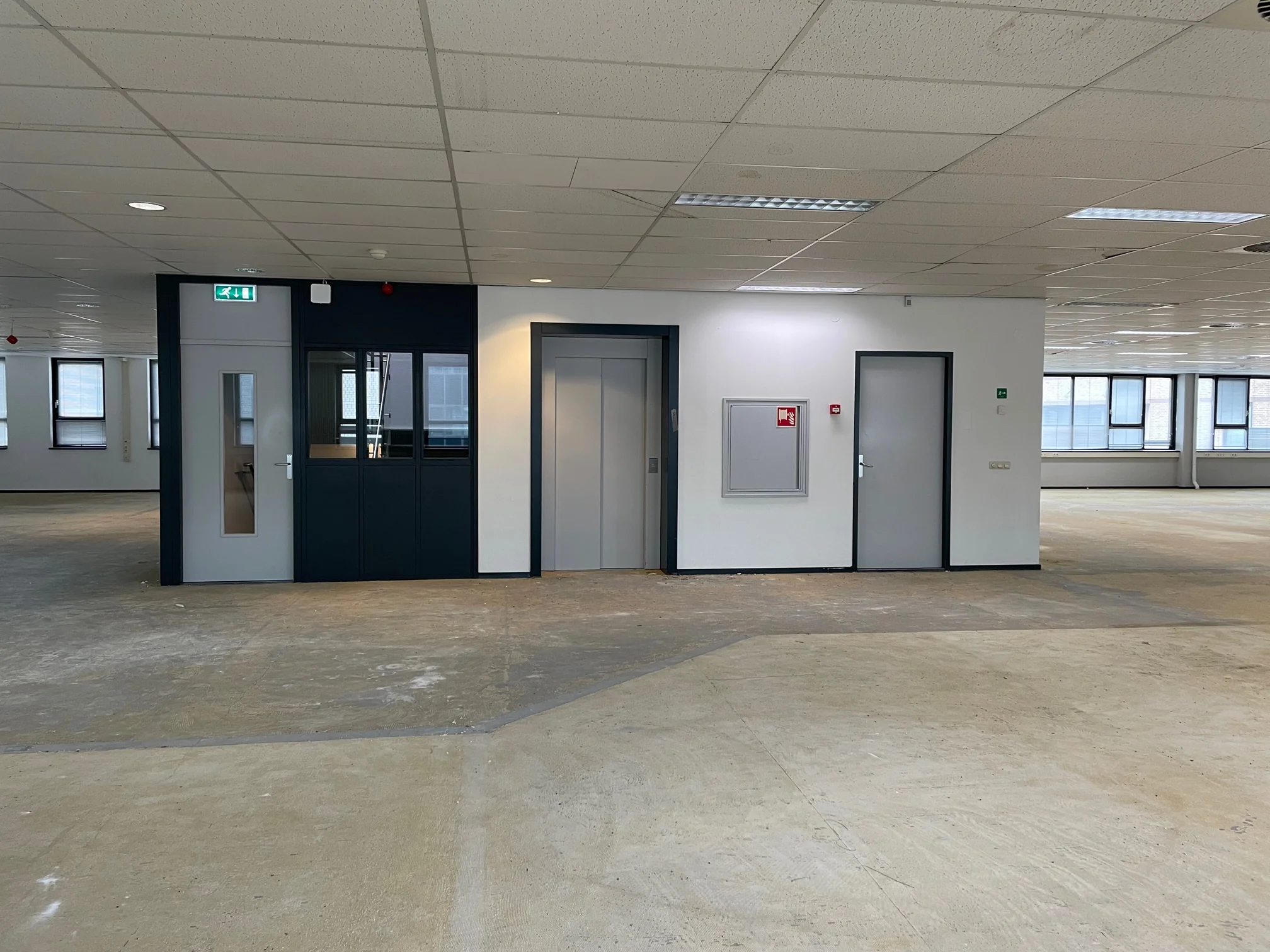 Leeg kantoorpand aan de Rivium 4e Straat met zicht op een lift, deuren en systeemplafond.